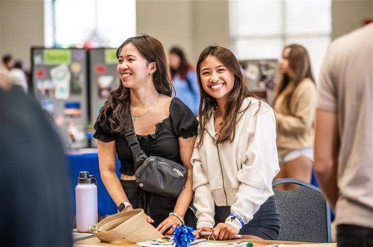 two women standing behind table at college fair